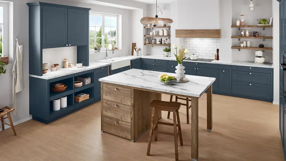 Cuisine en L aux meubles bleu marine avec plans de travail et îlot effet marbre blanc, sur un caisson d’îlot en bois