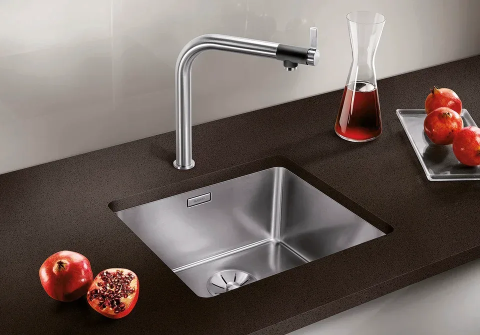 Évier en inox sous-plan dans un plan de travail brun foncé à grain fin, avec mitigeur en inox