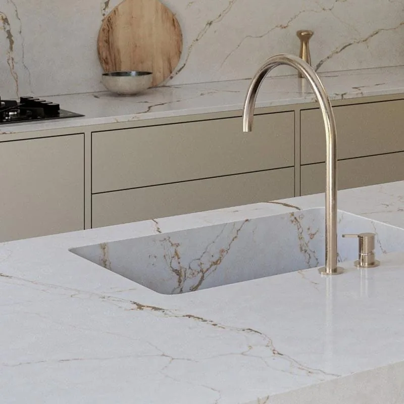Plan de travail en quartz blanc veiné d’or avec évier intégré, robinetterie dorée et crédence assortie