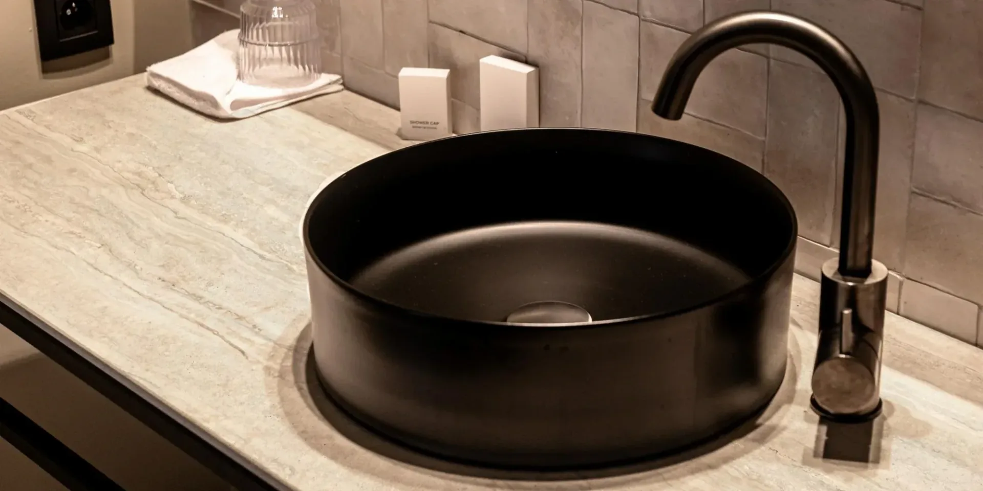 Vasque ronde noire mate posée sur un plan vasque clair veiné, avec robinet noir, dans une salle de bain carrelée